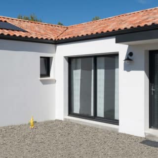 Maison neuve en Loire-Atlantique – façade avant avec porte d’entrée noire et enduit gratté blanc