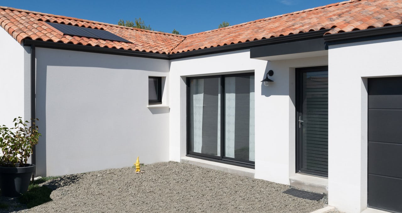 Maison neuve en Loire-Atlantique – façade avant avec porte d’entrée noire et enduit gratté blanc