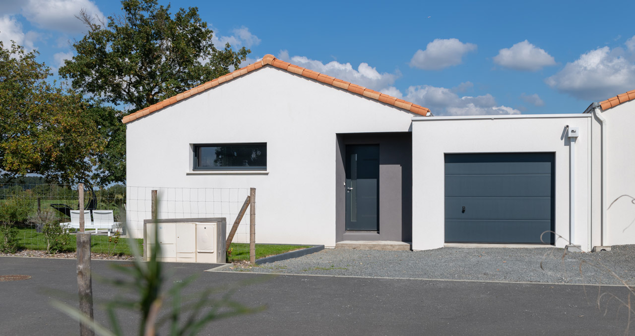 Entrée et façade avant d’une maison neuve avec enduit blanc et toiture en tuile Mêlé Atlantique.